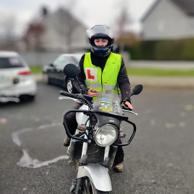 Learner rider in hi-vis and helmet sitting on a training motorcycle
