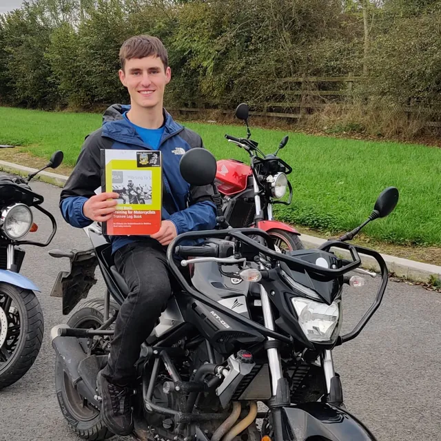 Rider holding the motorcycle theory test book while sitting on a bike